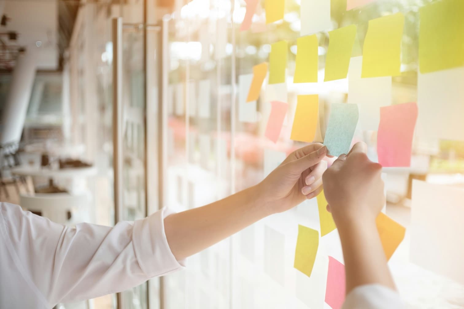 Des mains disposent des notes de couleur sur une paroi vitrée lors d'un atelier collectif d'évaluation des risques professionnels